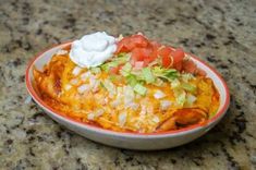 a bowl filled with taco salad on top of a granite counter next to a cup of sour cream