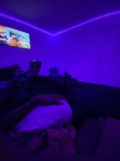 a person is laying in bed with purple lights on the wall and television above them