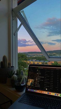 an open laptop computer sitting on top of a wooden desk in front of a window