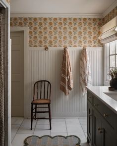 a chair sitting next to a sink in a bathroom under two towels hanging on the wall