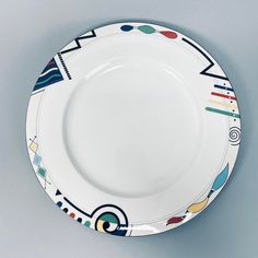 a white plate with multicolored designs on the rim is shown against a gray background