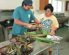 two people in a kitchen preparing food on trays and cutting up leafy vegetables