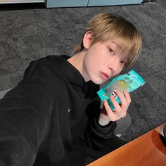 a boy sitting on the floor looking at his cell phone and holding it up to his face