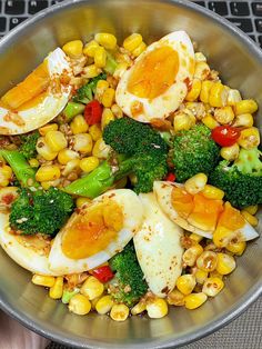 a metal bowl filled with corn, broccoli and hard boiled eggs