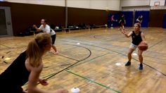 two women playing basketball in an indoor gym with other people sitting on the floor watching