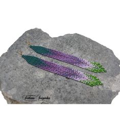 two purple and green beaded earrings sitting on top of a gray rock next to a stone