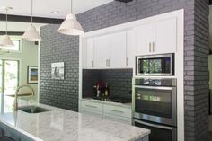 a kitchen with white cabinets and grey brick walls, an island countertop and two ovens