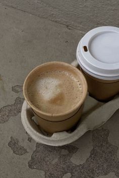 two coffee cups sitting on top of each other in front of a cement wall and floor