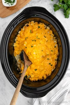 a wooden spoon in a black crock pot filled with macaroni and cheese