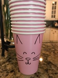 a stack of pink cups with a cat face painted on it's side, sitting on a kitchen counter