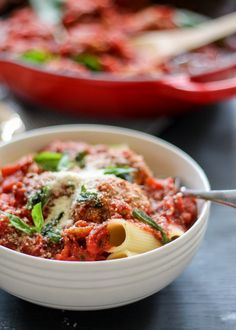 a white bowl filled with pasta and meat sauce next to a red casserole dish