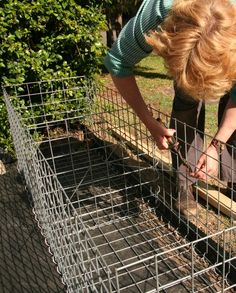 a woman is bending over to look at something in a metal cage on the ground