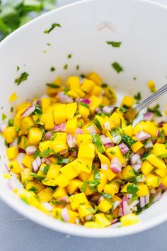 a white bowl filled with mango salsa and cilantro on top of a table