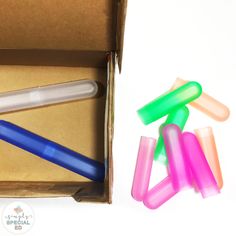 several different colored plastic pens in a box next to it's cardboard package with the lid open