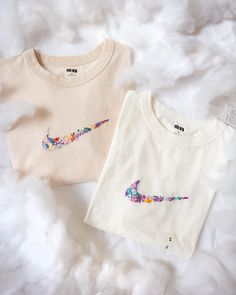 two white t - shirts with colorful designs on them sitting on a fluffy surface next to each other