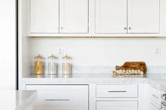 a kitchen with white cabinets and marble counter tops