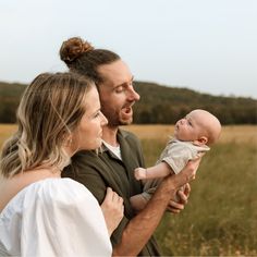 a man and woman holding a baby in a field