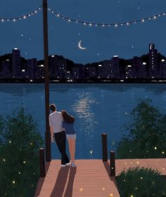 two people are standing on a dock looking at the water and city lights in the distance