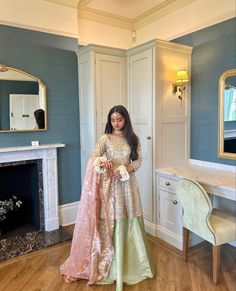 a woman standing in front of a fireplace wearing a long dress and holding a bouquet