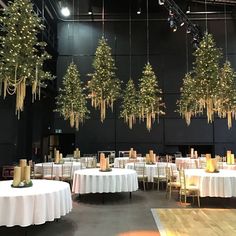 tables and chairs are set up with white tablecloths, gold candles and christmas trees hanging from the ceiling