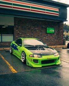 a green sports car parked in front of a building with its hood up and the hood down