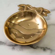 a golden metal bowl on a marble countertop with a gold bow and bead decoration