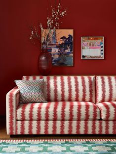 a red and white striped couch in front of a red wall with pictures on it