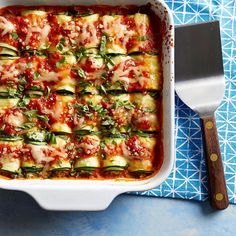 a casserole dish filled with zucchini and sauce on a blue tablecloth