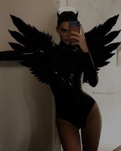 a woman in a black bodysuit with wings on her back taking a selfie