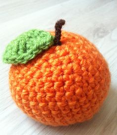 an orange crocheted with a green leaf sitting on top of a wooden table