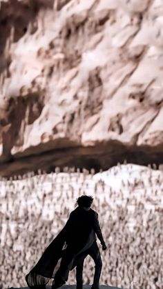 a man standing on top of a snow covered slope next to a large rock formation