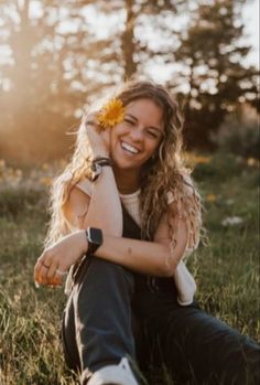 a woman sitting in the grass with a flower in her hair smiling at the camera