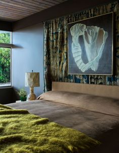 a bed in a bedroom next to a window with green carpet on the floor and a painting hanging above it