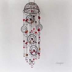 a metal wind chime with red beads hanging from it's side on a white wall