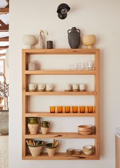 a wooden shelf filled with cups and bowls on top of it's sides next to a vase