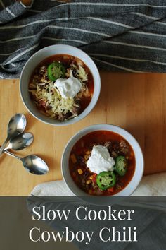 two bowls of slow cooker cowboy chili with sour cream on top and spoons