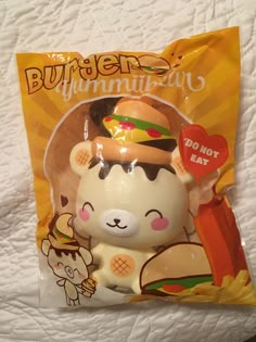 a stuffed animal with a burger on it's head in a package that is sitting on top of a bed