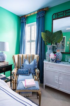 a bedroom with green walls, blue curtains and striped chair in front of the window