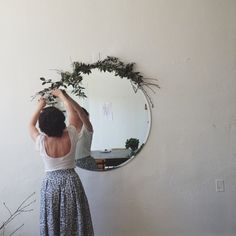 a woman in a dress is looking at herself in the mirror with greenery on it