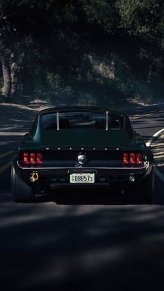 the rear end of a car driving on a road with trees and bushes in the background