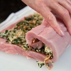 a person is cutting meat into pieces on a white plate with greens and seasoning