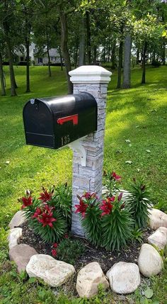 a mailbox in the middle of a flower bed with rocks around it and flowers