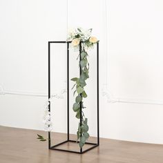 a vase with flowers and greenery in it on a wooden floor next to a white wall