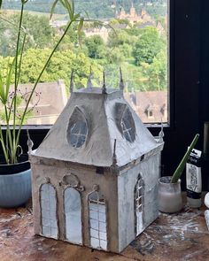 a doll house sitting on top of a table next to a potted plant in front of a window