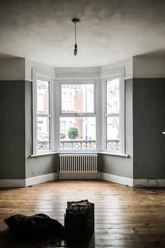 an empty room with hard wood flooring and large windows in the corner, including a radiator