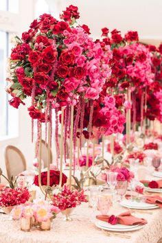 the table is set with pink and red flowers in tall vases on each side