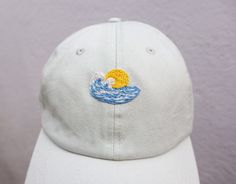 a white baseball cap with an embroidered sun and waves on it