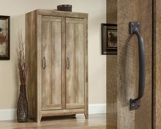 a tall wooden cabinet sitting in the corner of a room next to a vase with flowers