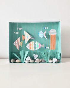 an origami fish and sea urchins in a green box with white rocks