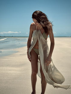 Long beach cover-up featuring a front overlay and adorned with resin beads and 24k gold-pleated details. The necktie and low back neckline add a touch of elegance, making it a perfect addition to your seaside wardrobe. Compliment this style with your favorite swimwear, an oversized straw bag, a hat, and sandals. Chic Gold Swimwear For The Beach, Elegant Halter Neck Beach Dress For Beach Party, Elegant Gold Swimwear For Beach, Gold Sleeveless Swimwear For Beach, Gold Halter Neck Swimwear For The Beach, Elegant Beach Dress For Beach Party, Elegant Beach Party Cover-up, Elegant Beach Dress For Beach Party Season, Elegant Beach Dress For Poolside